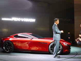 在概念车Mazda RX-VISION的车前接受采访的小饲雅道社长
